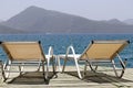 Sea resort, two empty deck chairs on a wooden pier on green mountains background Royalty Free Stock Photo