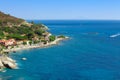 Sea shore with beach and rocks and rocky slope of the Island of Elba in Italy. Many people on the beach sunbathing. Blue sea with