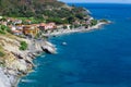 Sea shore with beach and rocks and rocky slope of the Island of Elba in Italy. Many people on the beach sunbathing. Blue sea with