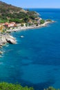 Seashore with beach and rocks and rocky slope of the Island of Elba in Italy. Many people on the beach sunbathing. Blue sea with