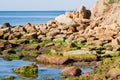 Sea shore, big coquina stones in water covered with green algae, reflections on water surface and little waves