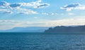The sea with the silhouette of a jagged rocky shore in the distance with mountains