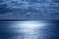 Sea and sky in the bottom half is a calm deep blue sea, on the horizon is a line of white shimmering glowing light from the moon