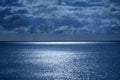 Sea and sky in the bottom half is a calm deep blue sea, on the horizon is a line of white shimmering glowing light from the moon