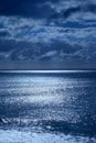 Sea and sky in the bottom half is a calm deep blue sea, on the horizon is a line of white shimmering glowing light from the moon