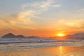 Sea with small waves, sand on the beach, mountains in the background, clouds from the sky, the sun sets, reflections in water and