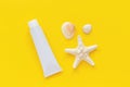 Sea starfish, seashells and white tube of sunscreen on yellow paper background. Mock up Template for lettering, text or your