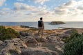 Sea sunset view. Man with backpack on rocks with beautiful view of Yeronisos Island near coast of Agios Georgios Pegeias Royalty Free Stock Photo