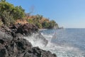 The sea surf breaks against a cliff of black lava boulders and water sprays high. Water drops fly through the air. The power. Royalty Free Stock Photo