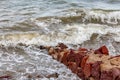 Sea water breaking over a small uneven reddish-brown stone wall on the beach Royalty Free Stock Photo