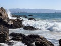 Sea water splash on rocks, algae and cargo ships by Valparaiso harbor