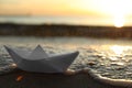 Sea wave carrying away white paper boat at sunset, space for text. Bokeh effect Royalty Free Stock Photo