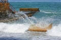 Sea wave crashed against a stone against the background of a concrete breakwater and the blue of the sea.