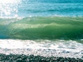 Sea wave with foam, beach, pebble, sun glare on the water, black