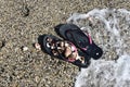 Sea wave splashes left on the beach black flip-flops with seashells.