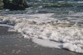 Sea wave spreading on the beach became sea foam near the rocks Royalty Free Stock Photo