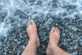 A sea wave on a stone beach covered with the rocks, male feet in the splashing wave. Royalty Free Stock Photo