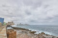 Sea waves breaking on a stone wall on the shore with buildings in the background on the Malecon in Cuba