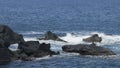 Sea waves clashing against rocks coming out from water, creating foamy splashes