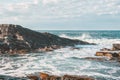 Sea waves crashing on rocks in sunny day against cloudy sky Royalty Free Stock Photo