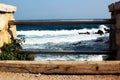 Sea waves hitting rocks behind handrail bars fixed between two brick posts Royalty Free Stock Photo