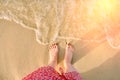 Sea waves near female feet. A woman in a red dress near the water by the ocean. The girl stands on the yellow sand by the sea, Royalty Free Stock Photo