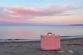 Seacoast with pink suitcases on the sandy beach on romantic sunset. Travel on holiday and tourist planning