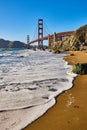 Seafoam on sandy beach with Golden Gate Bridge in background