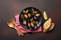 Seafood mussels and basil leaves in a black plate with towel, bread slices, wooden spoon and fork on rusty background Royalty Free Stock Photo