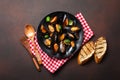 Seafood mussels and basil leaves in a black plate with towel, bread slices, wooden spoon and fork on rusty background Royalty Free Stock Photo