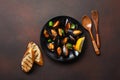 Seafood mussels and basil leaves in a black plate with towel, bread slices, wooden spoon and fork on rusty background Royalty Free Stock Photo