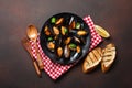 Seafood mussels and basil leaves in a black plate with towel, bread slices, wooden spoon and fork on rusty background Royalty Free Stock Photo