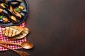 Seafood mussels and basil leaves in a black plate with towel, bread slices, wooden spoon and fork on rusty background Royalty Free Stock Photo