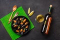 Seafood mussels, basil leaves in a black plate with wine bootle, wineglass, lemon, wooden spoon and fork on green bamboo mat and Royalty Free Stock Photo