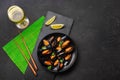 Seafood mussels, basil leaves in a black plate with wineglass, lemon and chopsticks on green bamboo mat and stone table