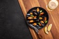 Seafood mussels and basil leaves in a black plate with wineglass, lemon, knife on wooden board and stone table