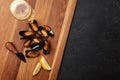 Seafood mussels and basil leaves in a black plate with wineglass, lemon, knife on wooden board and stone table.