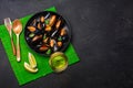 Seafood mussels, basil leaves in a black plate with wineglass, lemon, wooden spoon and fork on green bamboo mat and stone table