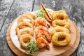 Seafood platter with deep fried squid rings, shrimp and onion rings decorated with lemon on cutting board on wooden background