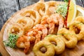 Seafood platter with deep fried squid rings, shrimp and onion rings decorated with lemon on cutting board on wooden background.