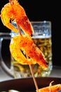 Seafood. Grilled fried shrimps on wooden skewers with spices and oil. On background of mug with beer, cast-iron frying pan. Royalty Free Stock Photo