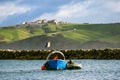 Sailors working on a boat in the water and a mountain in the background on a cloudy day with blue sky