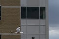 Seagull flying in front of beige brick building - cloudy gray sky - white bird with black wingtips - window with white panels Royalty Free Stock Photo
