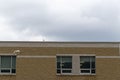 Seagull flying in front of beige brick building - cloudy gray sky - white bird with black wingtips - window with white panels Royalty Free Stock Photo