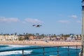 Seagull flying over ocean by railing of pier with landscape of beach in background. Royalty Free Stock Photo