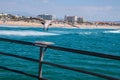 Seagull landing on bait cutting shelf on railing of pier with ocean and beach in the background. Royalty Free Stock Photo