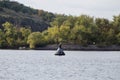 A seagull sits on a buoy in the middle of the river.