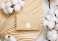 Sealed envelope on dried palm leaf with cotton flowers top view, wedding mockup