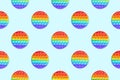 Seamless pattern of round rainbow silicone children`s toys antistress pop it or simple dimple on both sides on a blue background