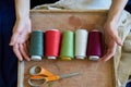 Seamstress or dressmaker keeps colorful spools of thread in hands on wooden background, top view